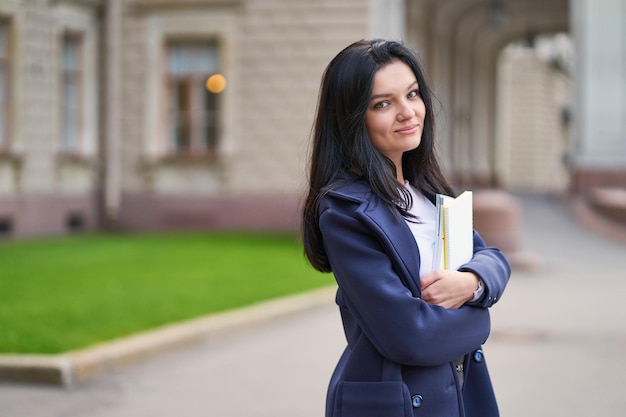 Photo portrait of young woman holding books outside university
