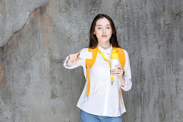 Portrait of young woman holding bottle of water and showing business card. High quality photo