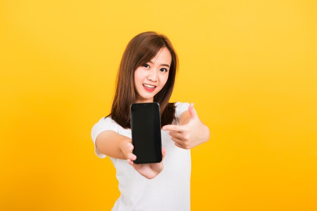 Portrait of young woman holding camera while standing against yellow background