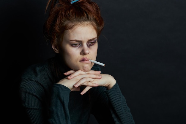 Portrait of young woman holding cigarette against black background