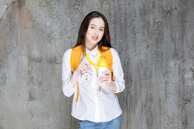 Portrait of young woman holding clock and water bottle. High quality photo