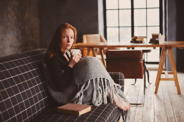 家のソファでリラックスしている若い女性がコーヒーカップを握っている肖像画