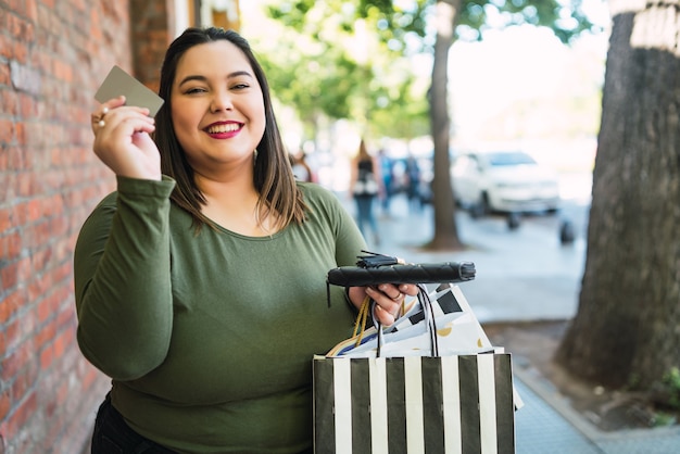 portrait of young woman holding a credit card and shopping bags outdoors on the street
