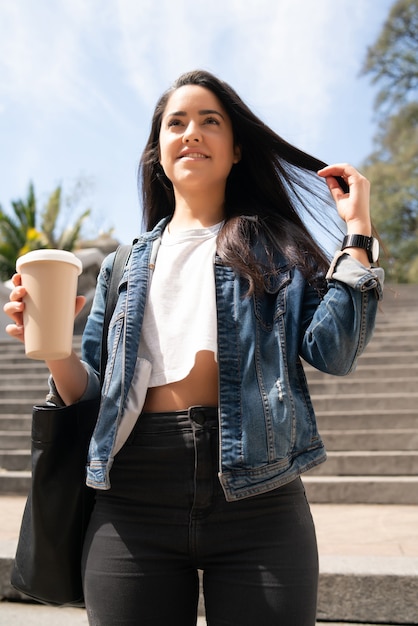 Portrait of young woman holding a cup of coffee while walking outdoors. Urban concept.