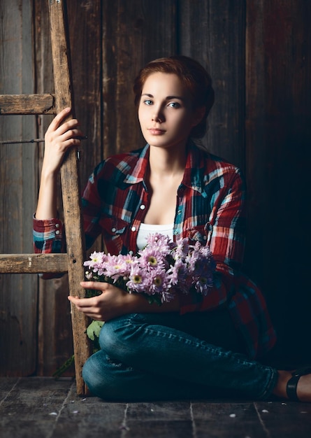 木製の背景に花を保持している若い女性の肖像画