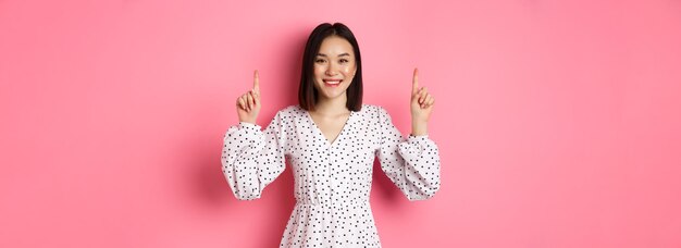 Portrait of young woman holding gift against pink background