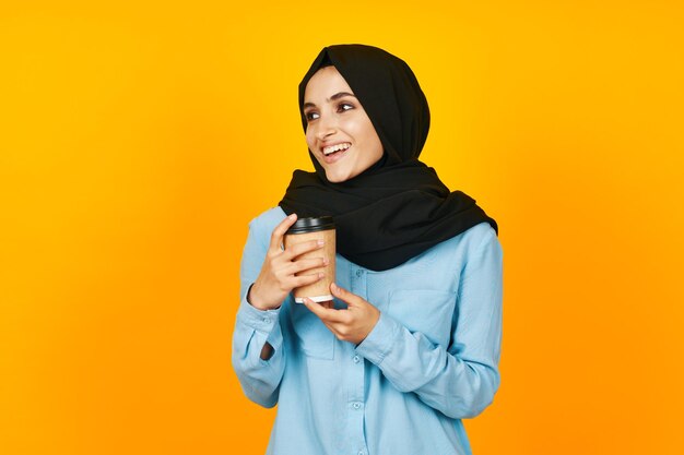 Portrait of young woman holding gift against yellow background