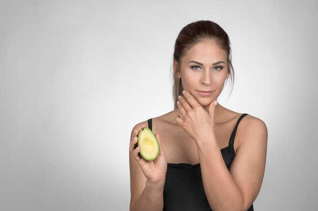 Foto ritratto di una giovane donna che tiene un avocado a metà su uno sfondo bianco