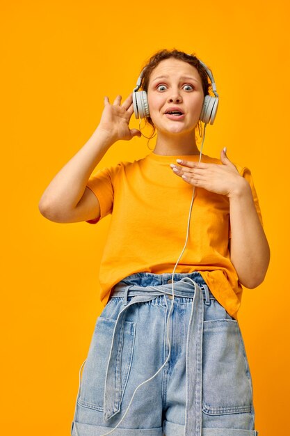 Portrait of young woman holding headphones while standing against yellow background