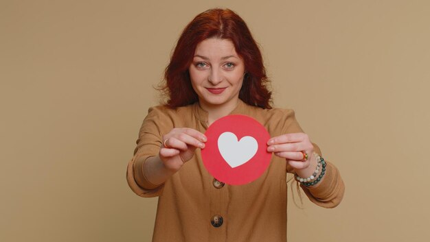 Photo portrait of young woman holding heart shape against pink background