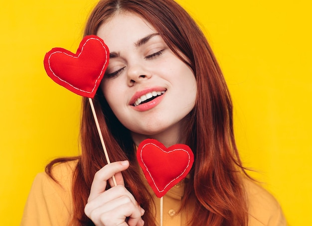 Portrait of young woman holding heart shape against yellow background