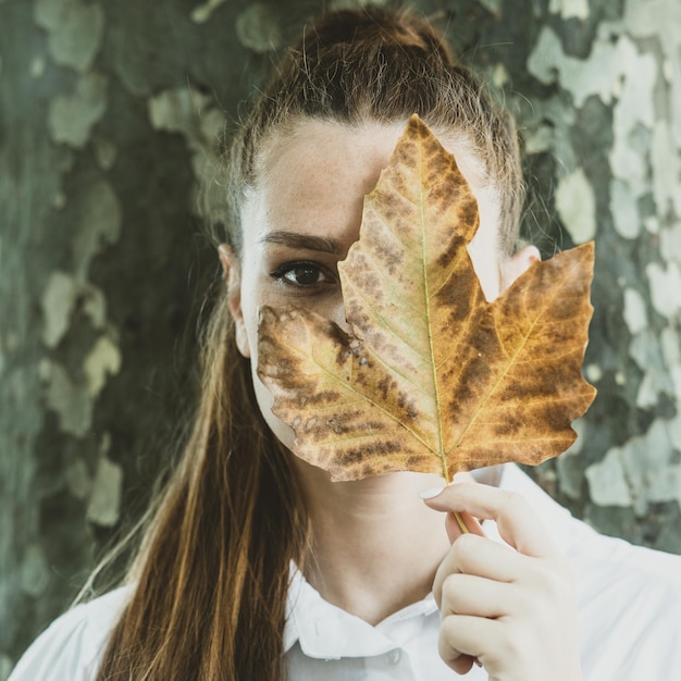 Foto ritratto di una giovane donna che tiene una foglia durante l'autunno