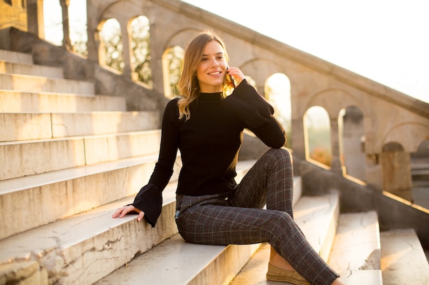 Portrait of young woman holding mobile phone while sitting on the stairs outdoor