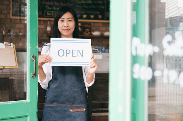 Portrait of young woman holding open sign while standing at doorway in cafe