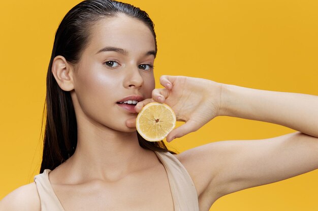 Photo portrait of young woman holding orange fruit against yellow background