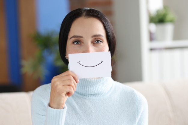 Photo portrait of young woman holding paper with painted smile. good mood and positive concept