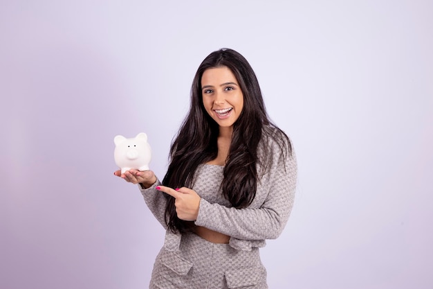 Portrait of young woman holding a piggy bank pointing at it