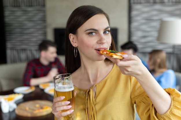 Ritratto di una giovane donna che tiene pizza e birra in un pub