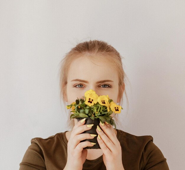 Portrait of young woman holding potted flowers against wall