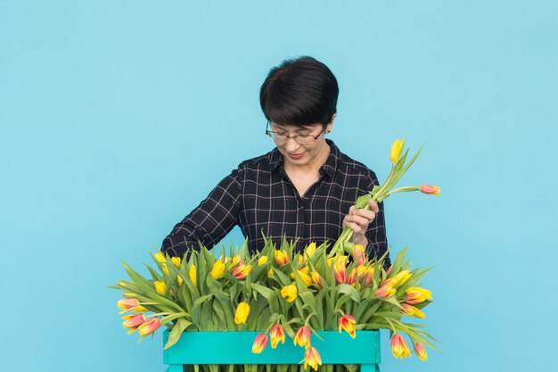 Portrait of young woman holding red flower against blue background