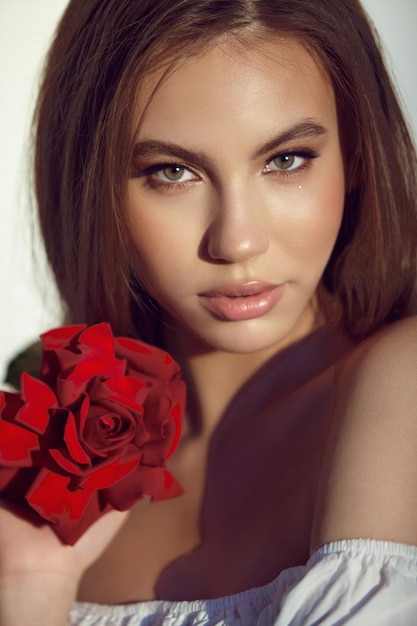 Portrait of young woman holding red rose on blurred background