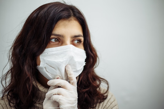 Portrait of young woman holds on her finger showing silence sign and has to stay home during quarantine due to coronavirus pandemia. Beautiful girl wearing medical mask and gloves. Covid-19 epidemia.