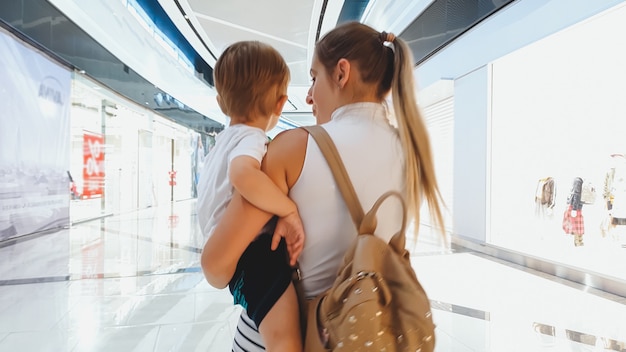 Portrait of young woman hugging her little son and walking in big shopping mall