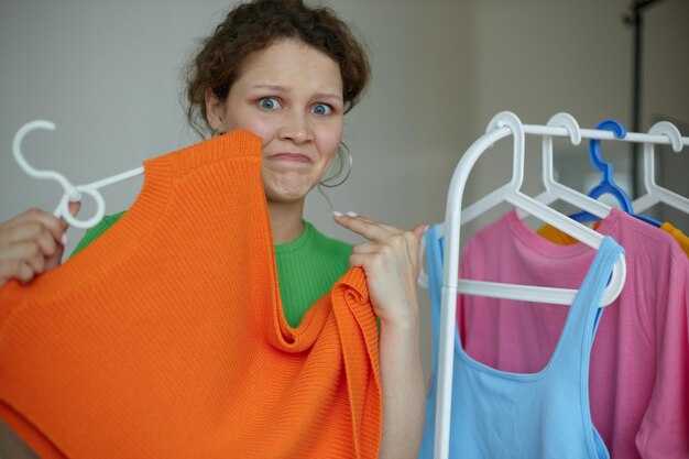 変更されていないハンガーのワードローブの明るい背景に服をアイロンをかける若い女性の肖像画