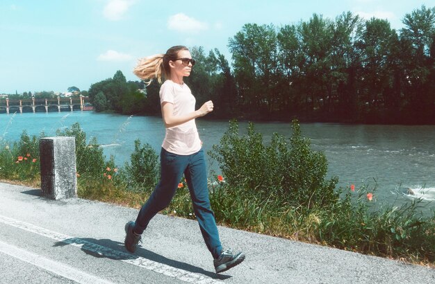 Portrait of young woman jogging by river against sky