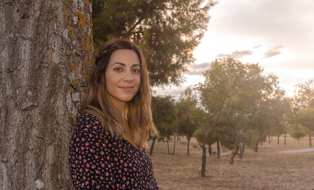 Portrait of young woman leaning against a tree in autumn. Selective focus.