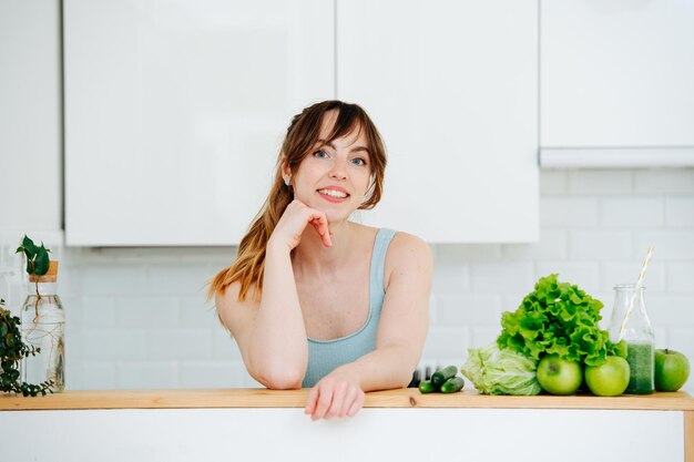 Portrait of a young woman leaning on a high kithen table next to pile of greens