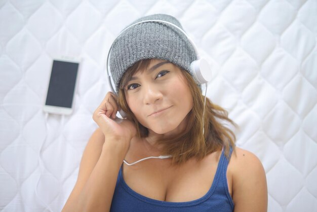 Photo portrait of young woman listening music while lying on bed at home