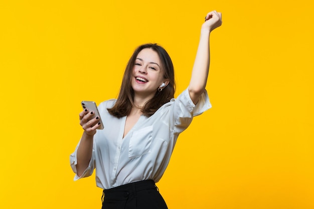 Portrait of a young woman listening to music with headphones and dancing on a yellow background