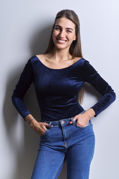 Ritratto di giovane donna che guarda l'obbiettivo su sfondo bianco. bella donna sorridente con un sano sorriso dentato bianco, capelli lunghi e lisci in abiti blu alla moda, jeans