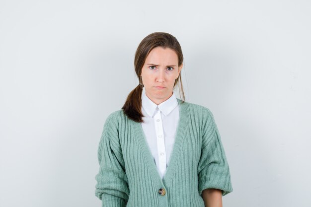 Portrait of young woman looking at front in blouse, cardigan and looking sulky front view