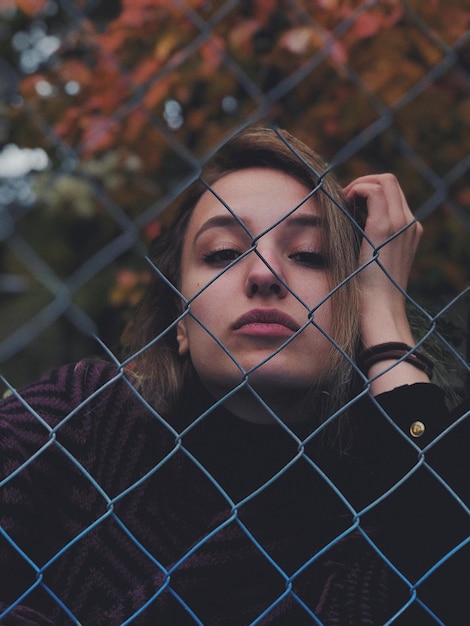 Photo portrait of young woman looking through chainlink fence