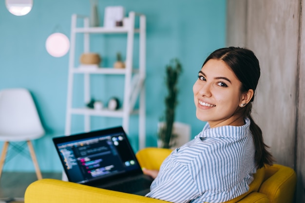 Portrait of young woman mobile developer with laptop, writes program code on a computer, programmer work.