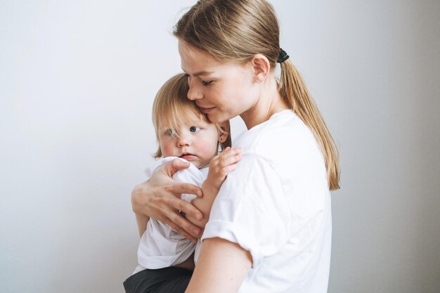 Portrait of young woman mother kissing baby girl daughter on hands at home