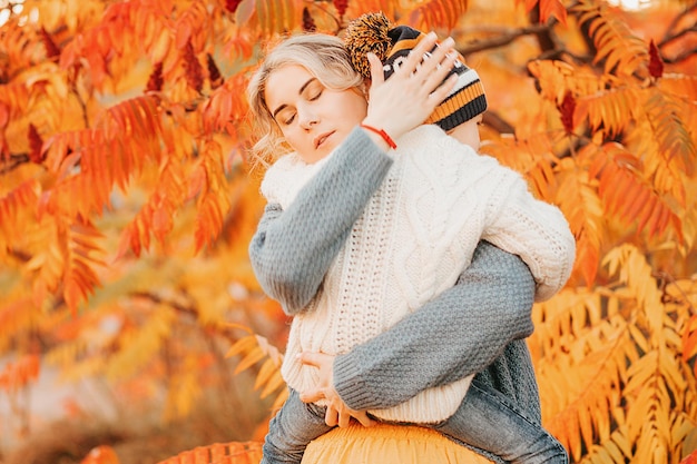 Photo portrait of young woman mother tightly pressed to breast child - boy of 4 years old. embracing, pities, soothes, protects. childish fears. autumn season. red - yellow foliage background. stress