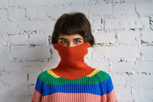 Portrait of a young woman in a multicolored sweater, covering her face with a sweater . The concept of shyness