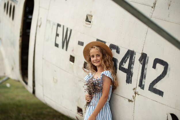 Portrait of a young woman near a retro airplane. in hat and flowers