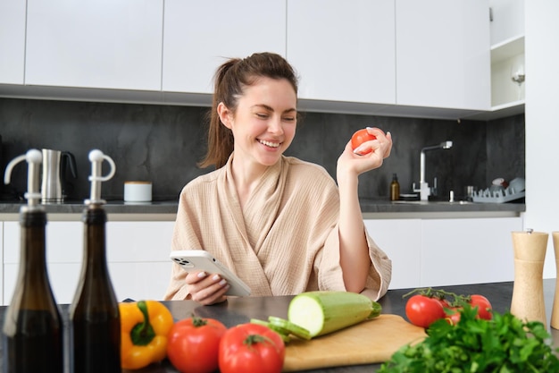 切り株の近くに座ってトマトを持ったスマートフォンのアプリで食料品を注文する若い女性のポートレート