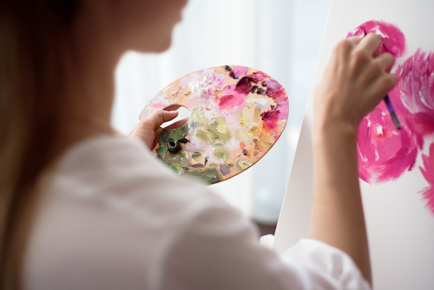 Portrait of a young woman painting with oil paints on white canvas, side view portrait