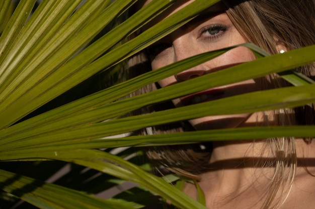 Portrait of young woman behind palm leaves cosmetic wellness skincare and summer spa fashion beauty