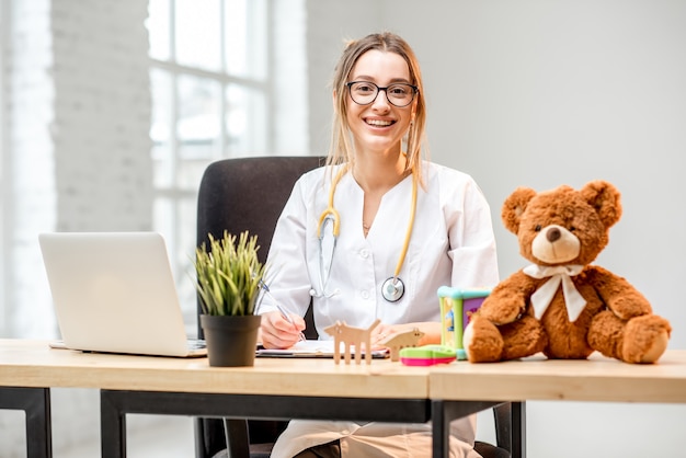 Portrait of a young woman pediatrician in medical gown sitting at the office