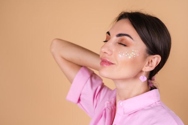 Portrait of a young woman in a pink dress   with shine glitter makeup and cute earrings posing positively 