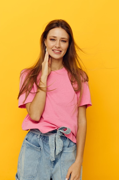 Portrait of a young woman pink tshirts and denim shorts posing yellow background