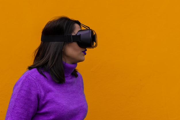 Portrait of a young woman playing with virtual reality goggles on a yellow background