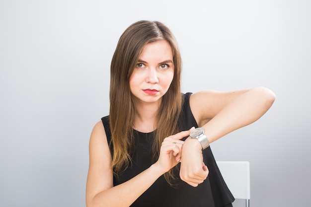 Portrait of a young woman pointing finger on wrist watch on a white background