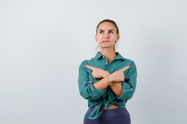 Photo portrait of young woman pointing to the opposite directions, biting lip in green shirt and looking pensive front view